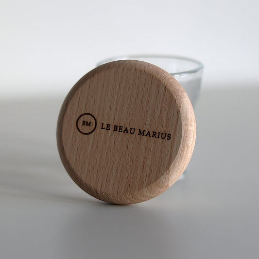 Décapsuleur aimanté en hêtre gravé Le Beau Marius, posé contre un verre