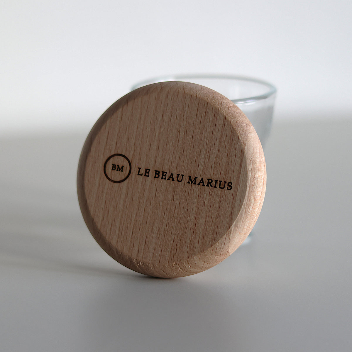 Décapsuleur aimanté en hêtre gravé Le Beau Marius, posé contre un verre